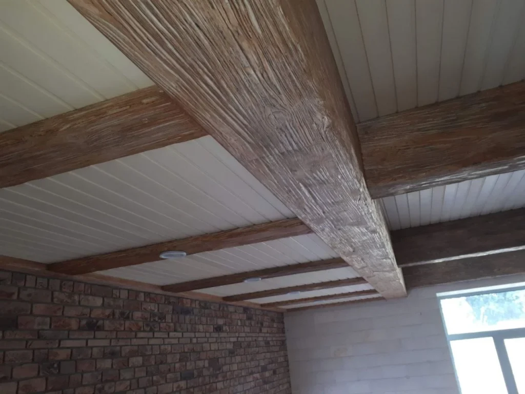 Exposed pale timber ceiling beams above a bare brick wall